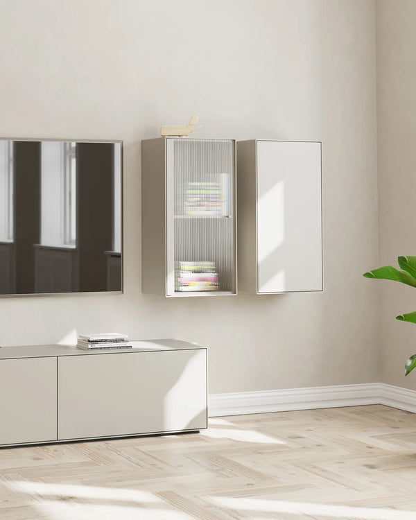 A modern wall-mounted storage cabinet system in a minimalist living room. The set includes a tall cabinet with frosted glass doors and open shelving, a matching tall cabinet with a solid door, and a low sideboard below with a wall-mounted TV.